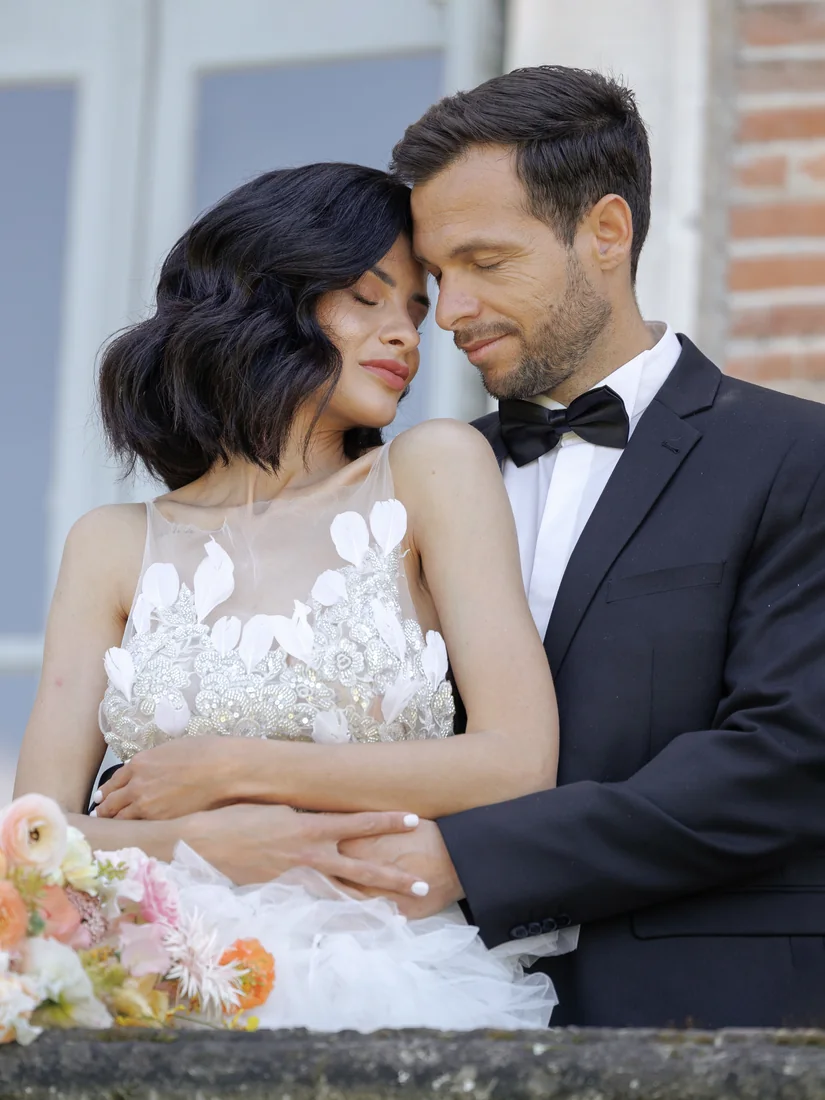 Les mariés front contre front, la mariée tenant un bouquet coloré