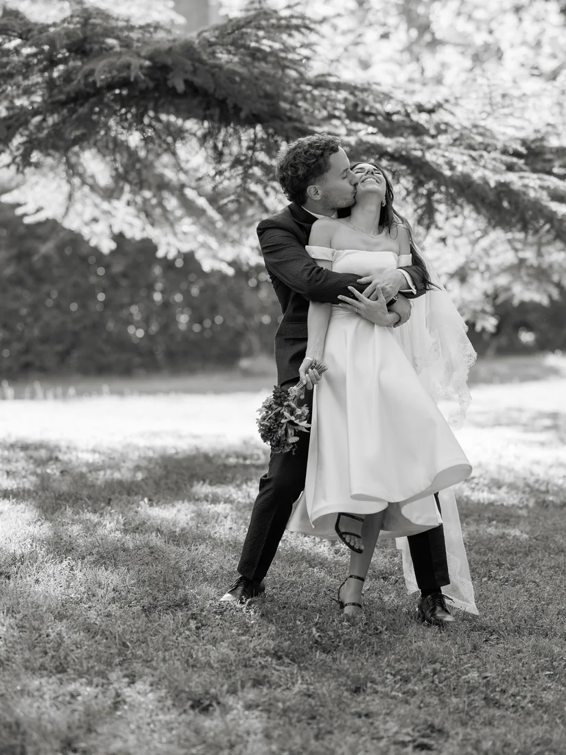 Le marié soulève la mariée sous un arbre, en noir et blanc