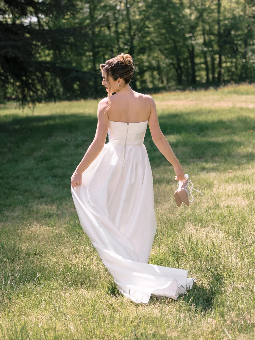 La mariée marche de dos dans un pré, son bouquet à la main