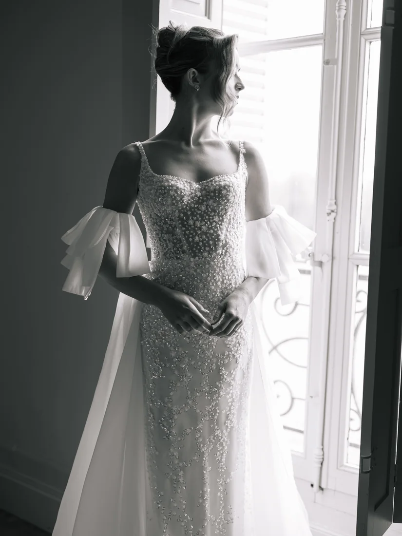 La mariée de profil devant une fenêtre, robe à volants, en noir et blanc