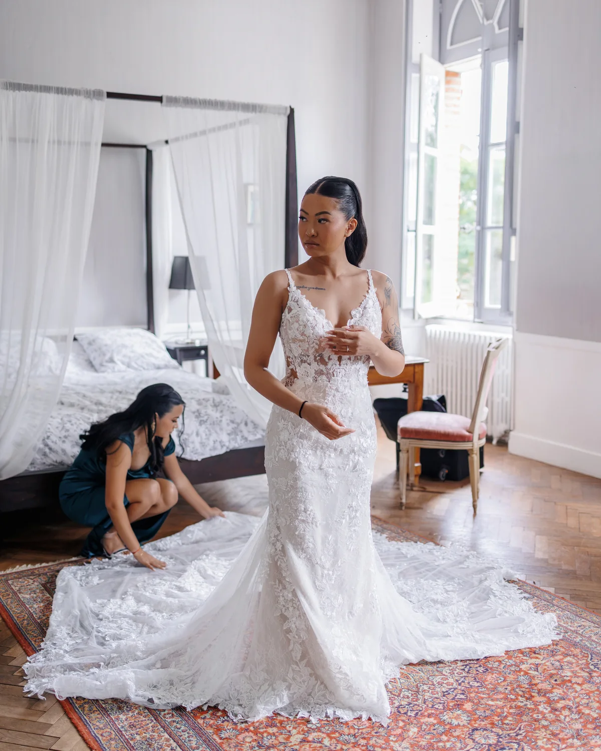 Une proche ajuste la traîne de la mariée dans la chambre, pendant les préparatifs