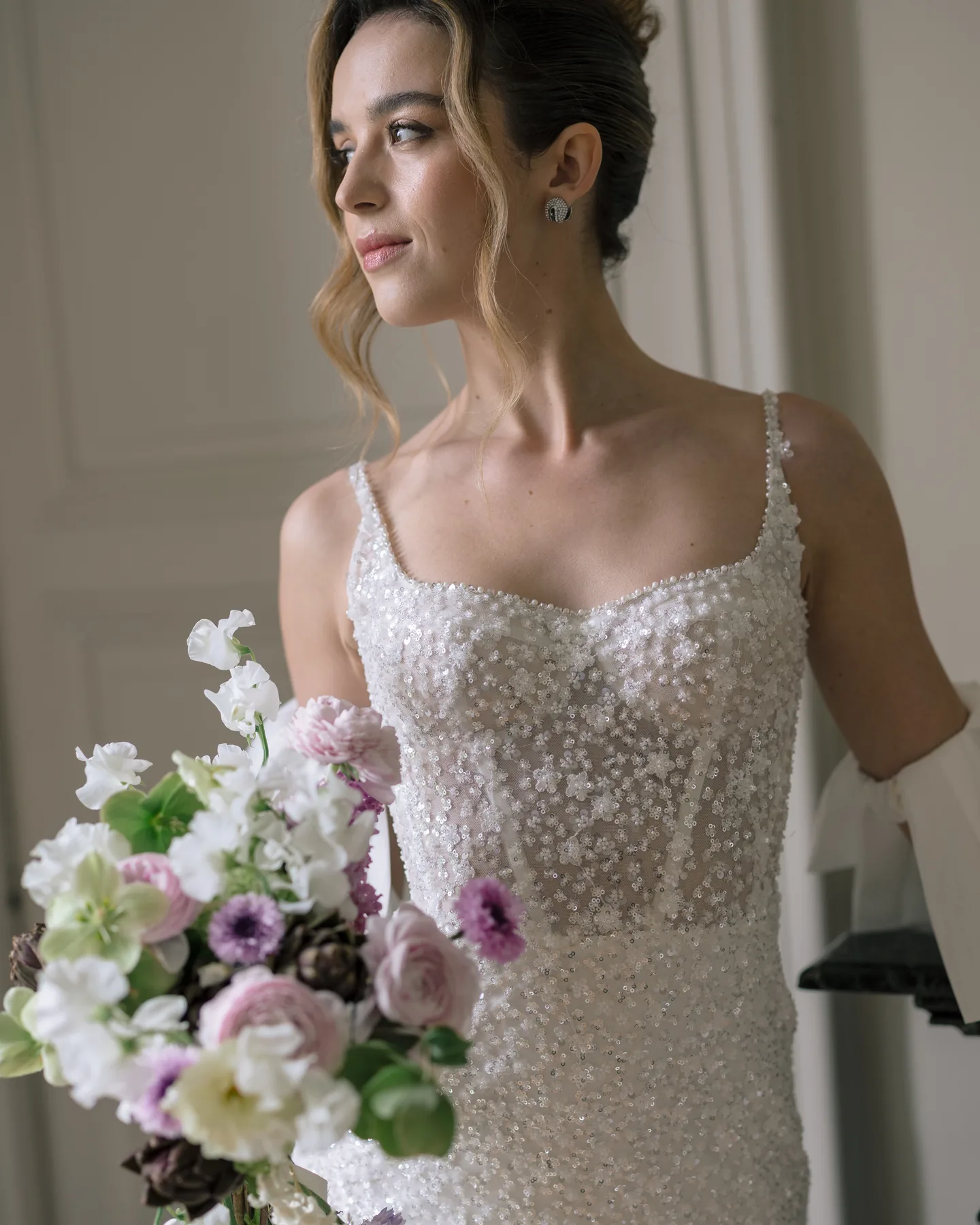 Mariée tenant un bouquet de fleurs de saison, robe brodée de perles