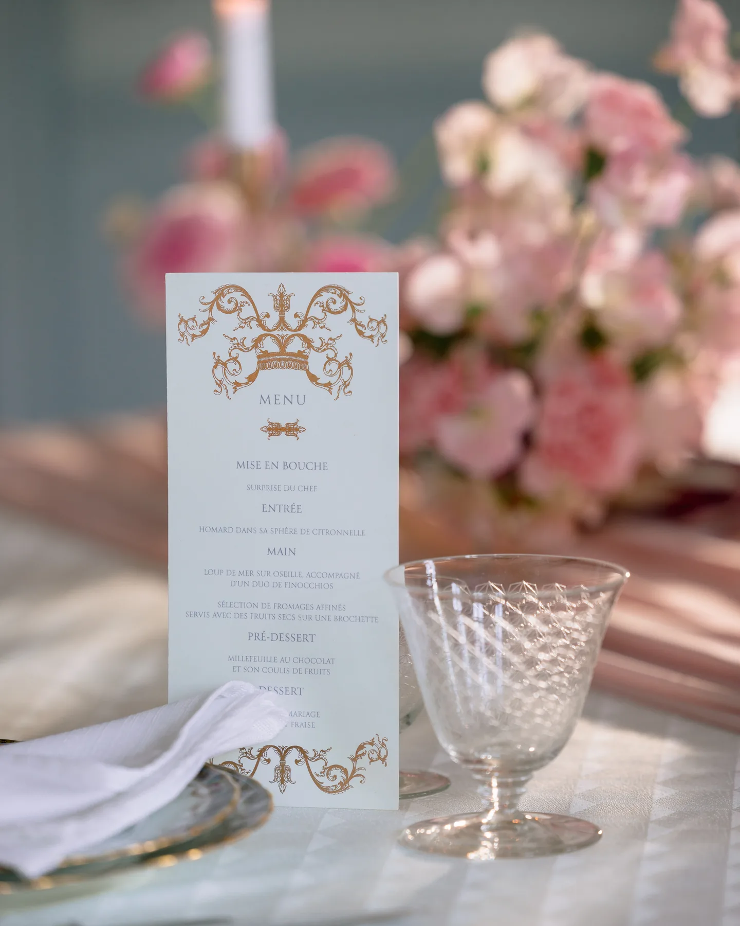 Menu calligraphié posé sur une assiette, entouré de fleurs roses