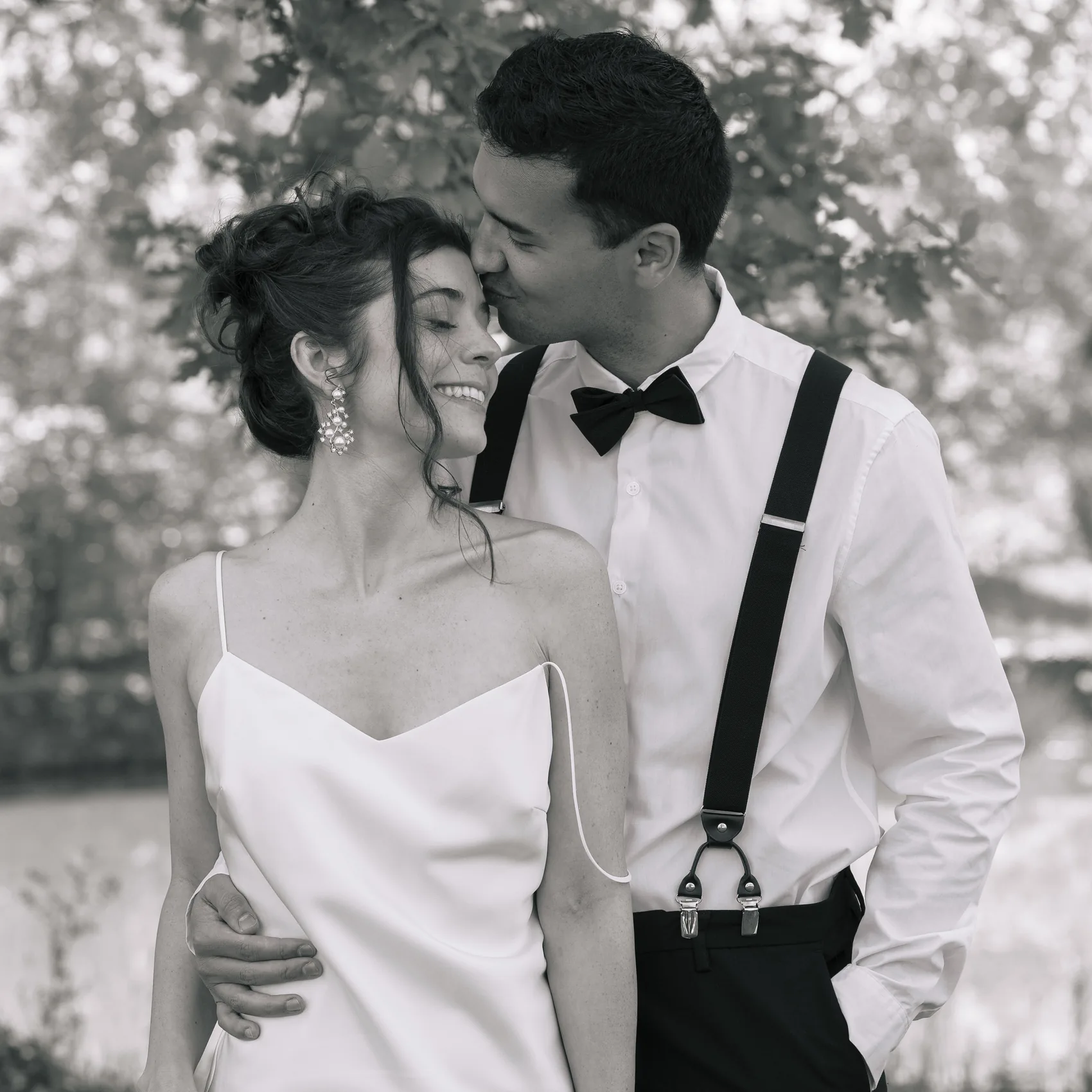 Le marié embrasse le front de la mariée, en noir et blanc
