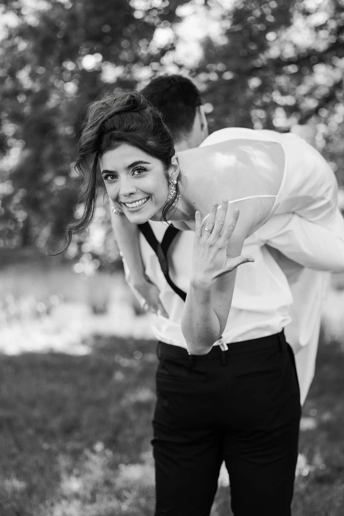 La mariée rit tandis que le marié se penche vers elle, en noir et blanc