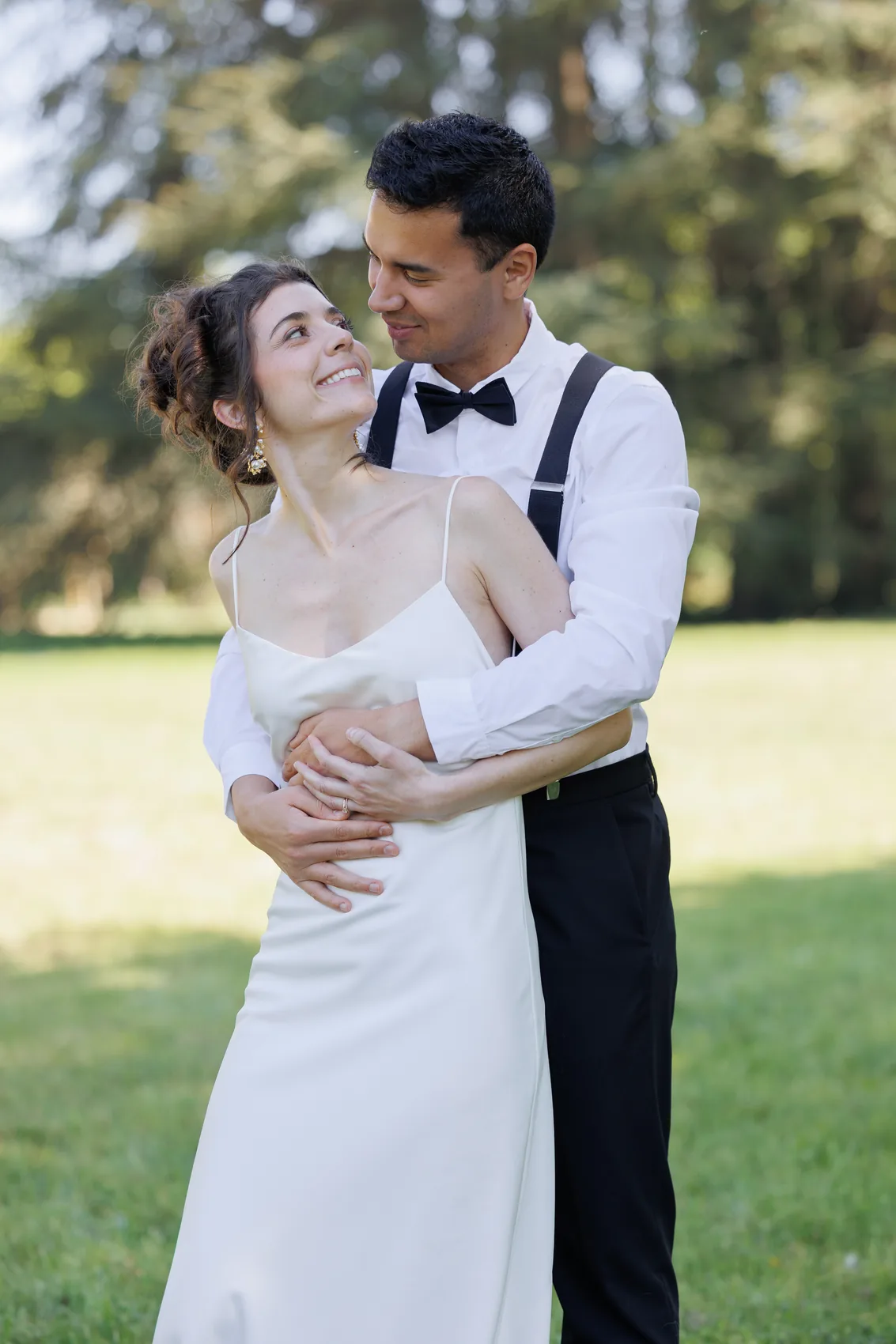 Le marié enlace la mariée par derrière dans l'herbe
