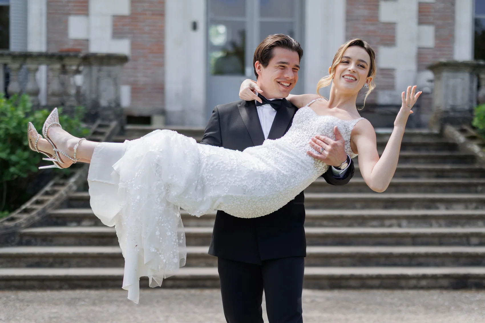 Le marié porte la mariée dans ses bras devant l'escalier d'un château