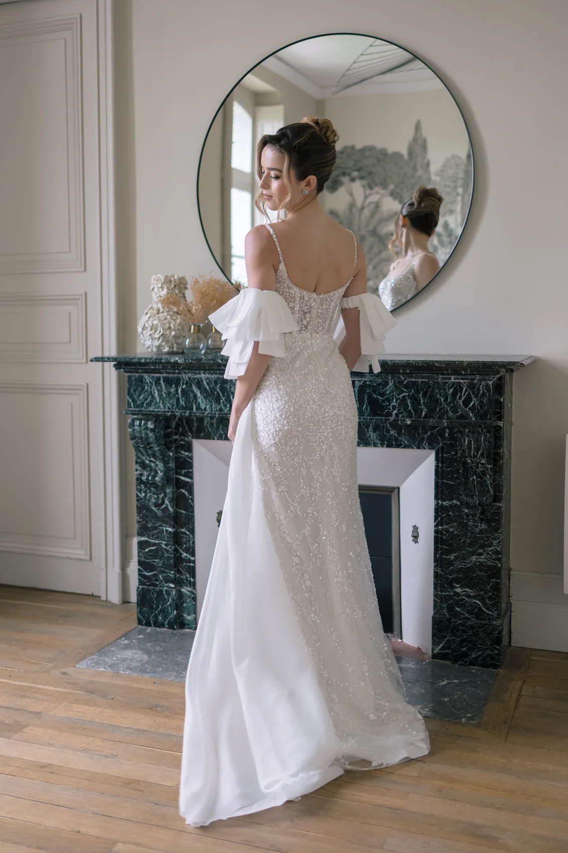 La mariée de dos devant un miroir rond, robe à volants