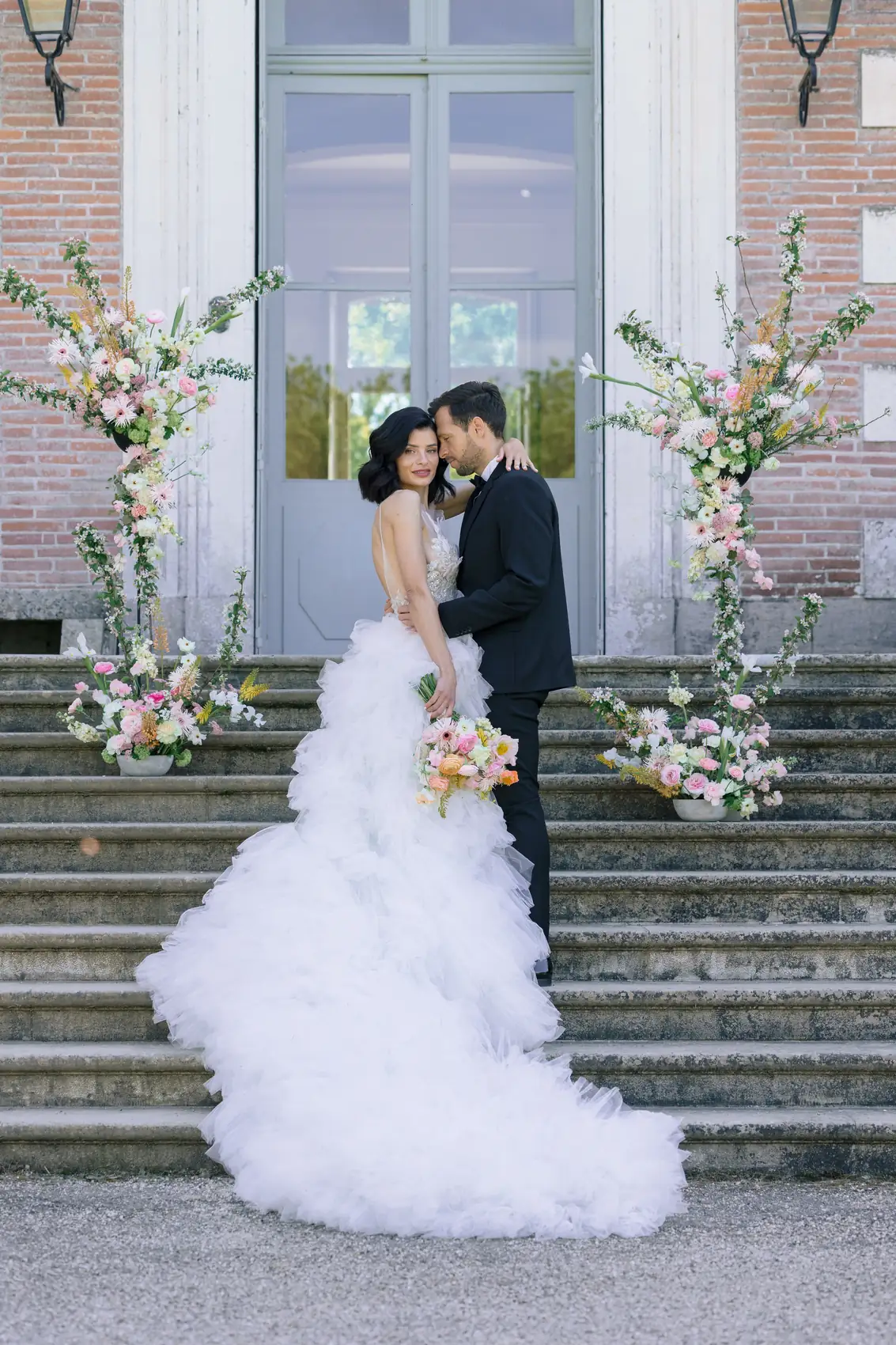 Les mariés en haut d'un escalier de pierre, longue traîne de tulle déployée