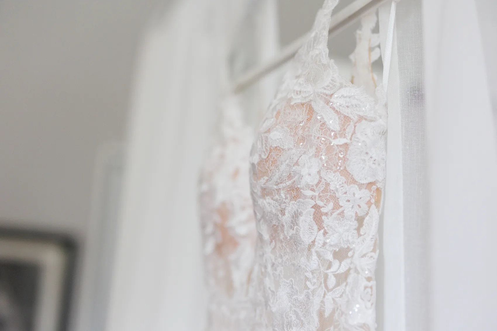 Robe de mariée en dentelle suspendue devant une fenêtre