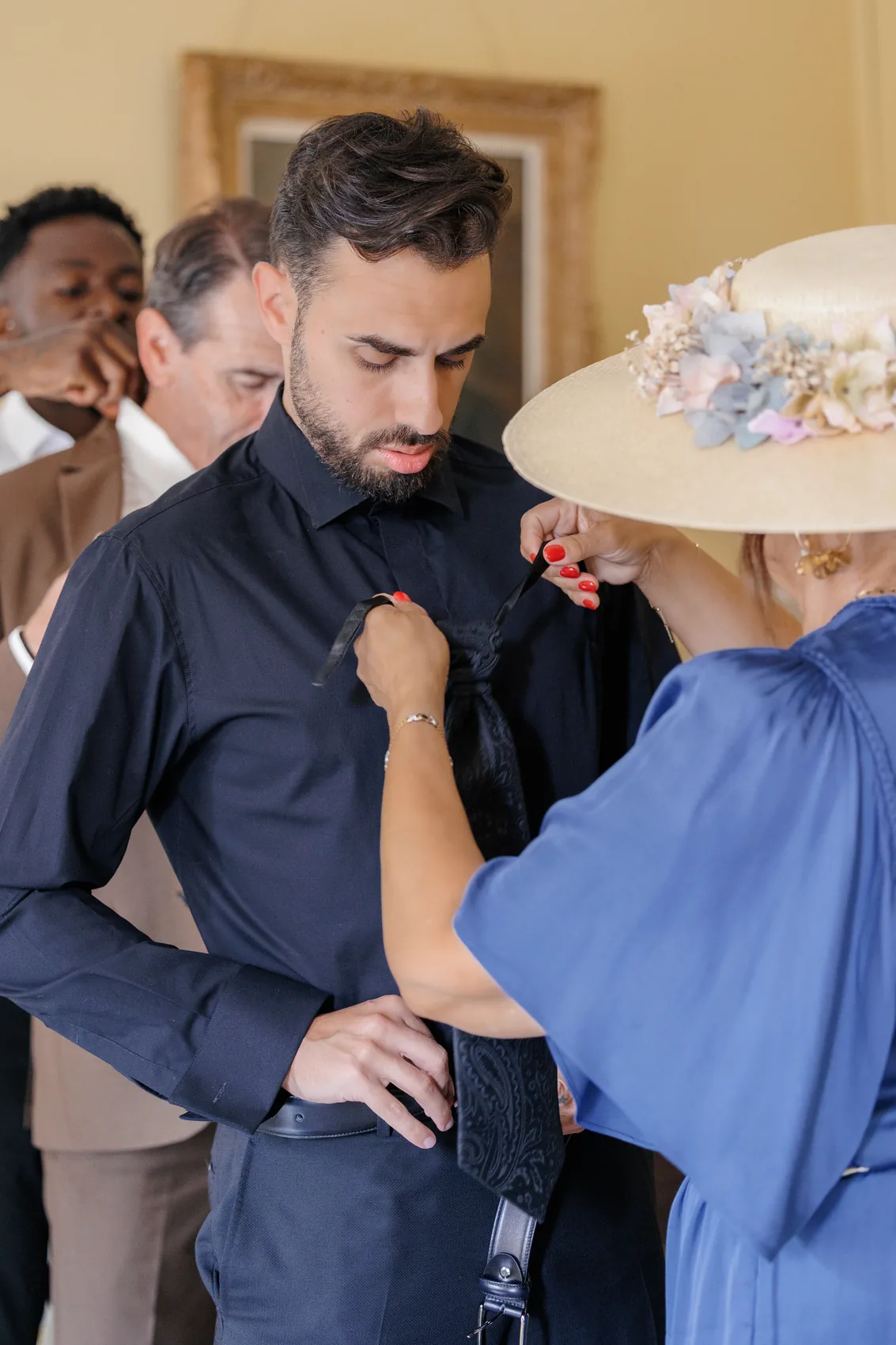 Le marié aidé à s'habiller par une proche coiffée d'un chapeau