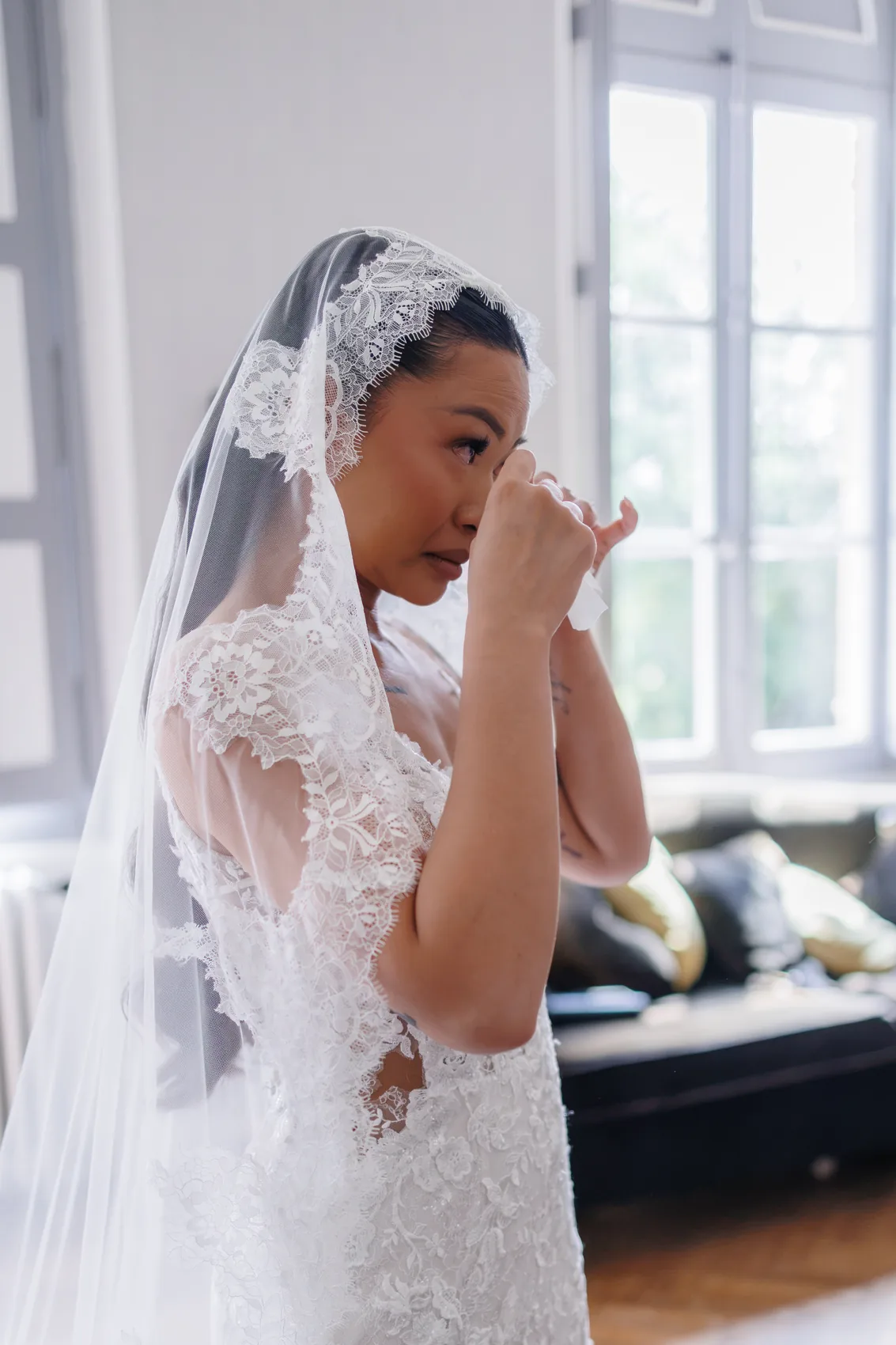 La mariée essuie une larme sous son voile de dentelle