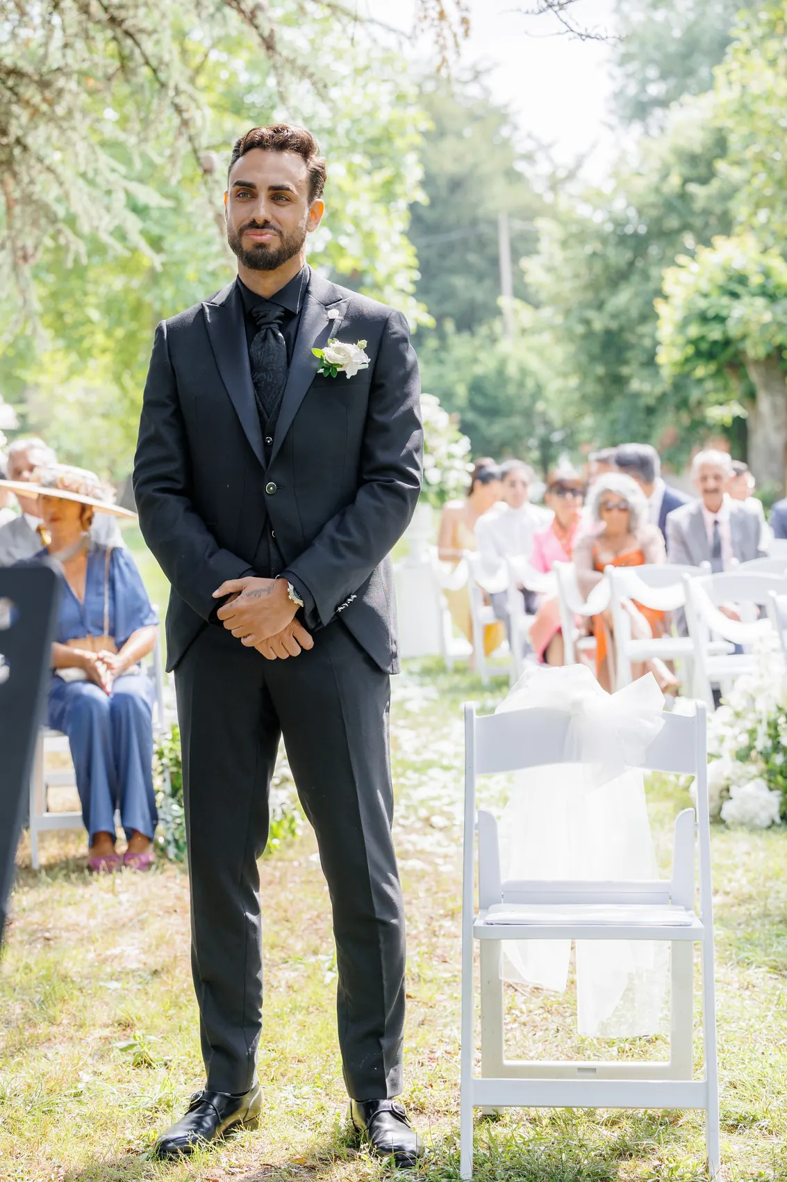 Le marié attend, mains jointes, devant les invités assis