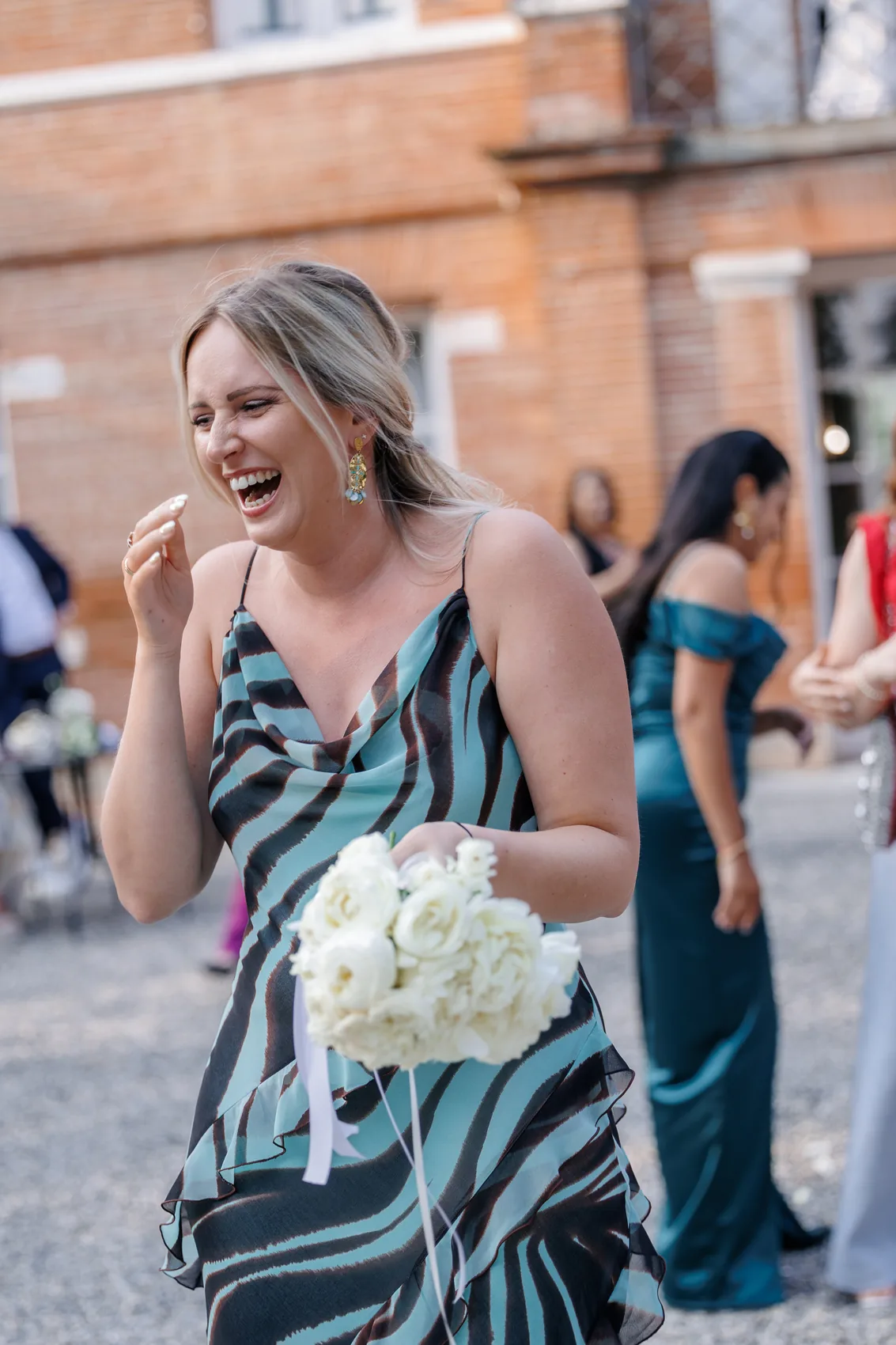Une invitée éclate de rire, un bouquet à la main, devant le domaine
