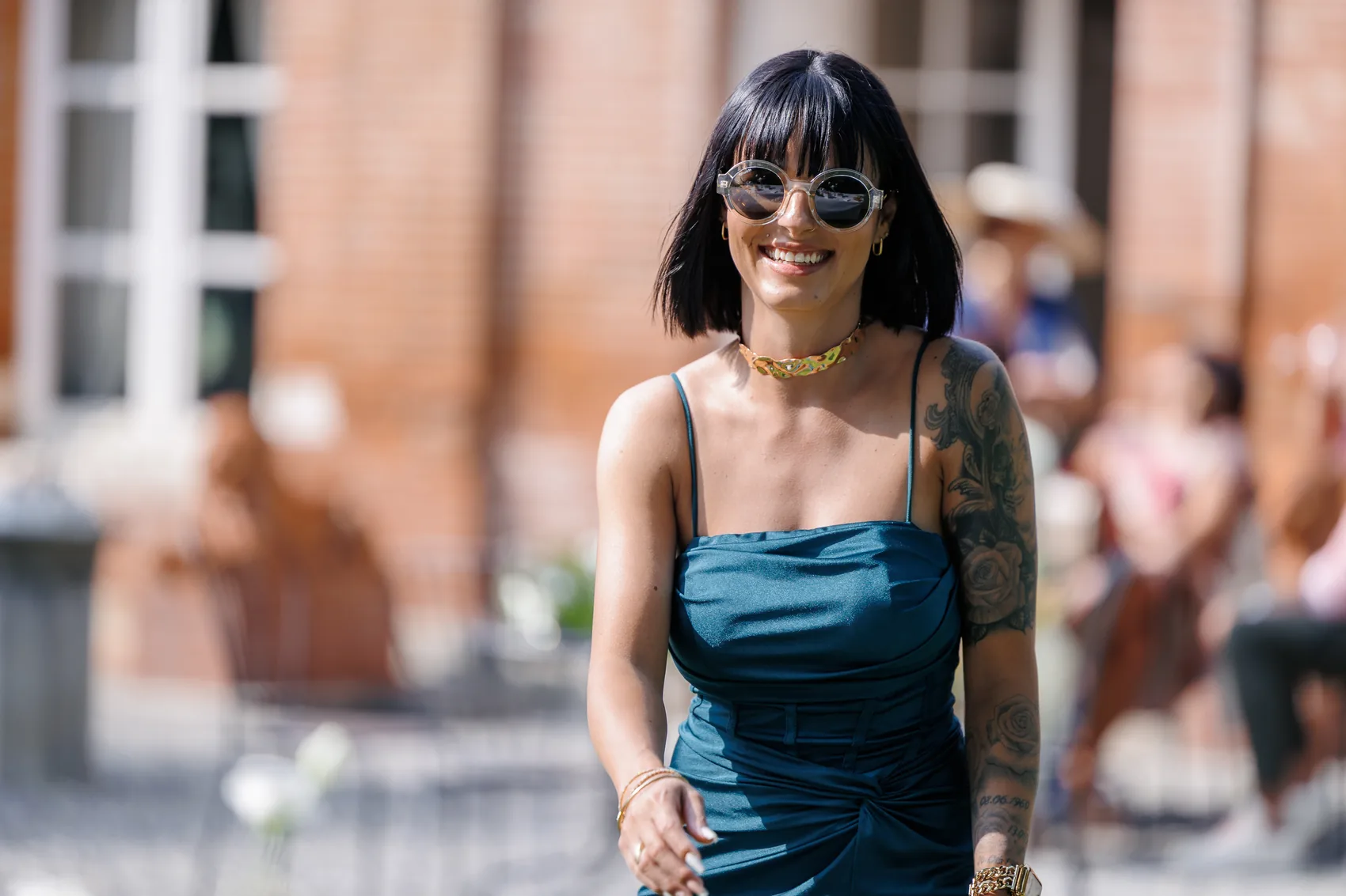 Une invitée souriante, lunettes de soleil, devant la façade en brique