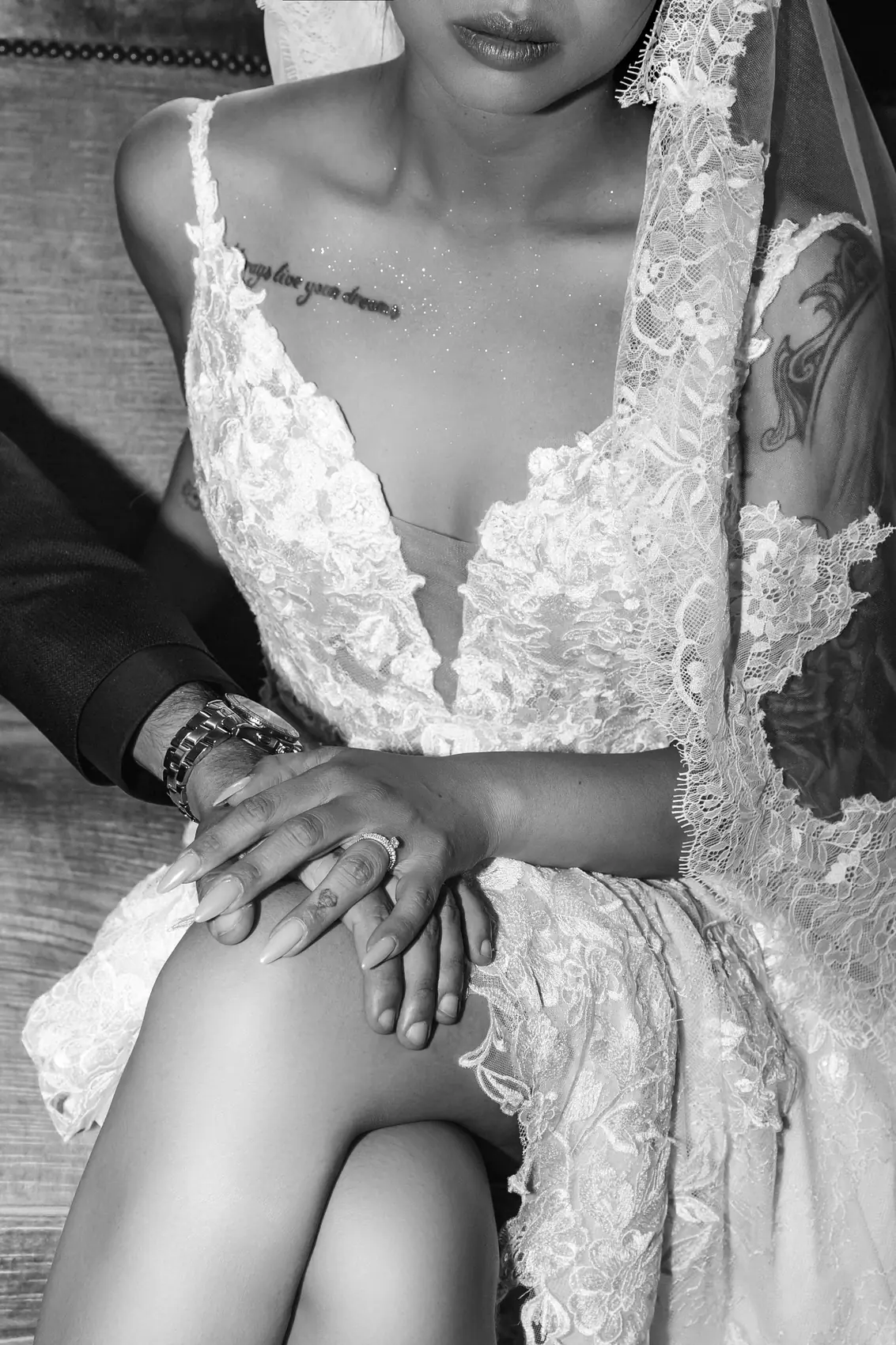 Les mains des mariés posées sur la dentelle de la robe, en noir et blanc